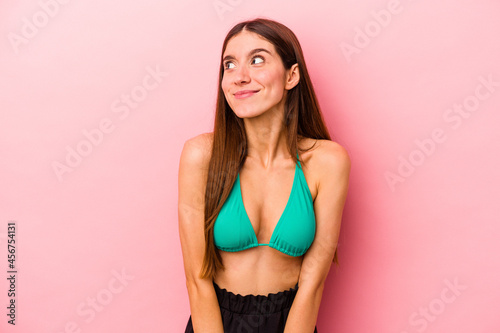 Young caucasian woman wearing bikini isolated on pink background dreaming of achieving goals and purposes