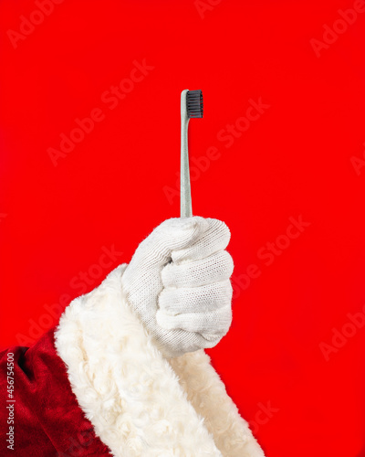 Close-up of Santa Claus's hand holding a toothbrush up.Concept of  healthy lifestyle, daily hygiene. Red background with copy space.