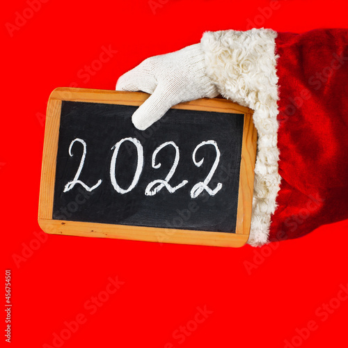 Close up Santa Claus's hand is holding a blackboard with the new year 2022 number written in chalk. New Year concept.