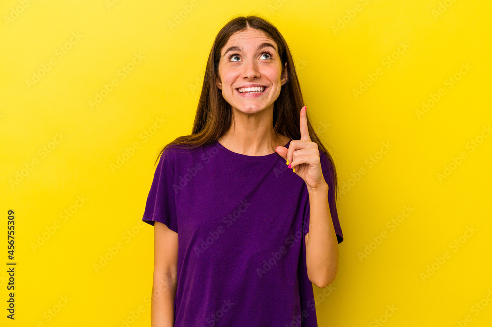 Young caucasian woman isolated on yellow background indicates with both fore fingers up showing a blank space. Young caucasian woman isolated on yellow background indicates with both fore fingers up showing a blank space.