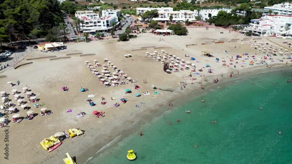 Aerial footage of the Spanish island of Ibiza showing the beautiful beach front on and the beach at Cala Llonga in the summer time in the Balearic Islands, Spain