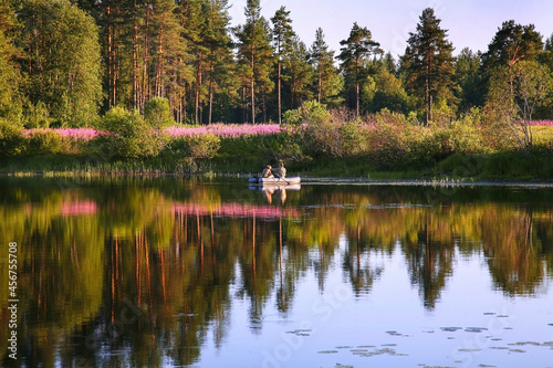 Two people in a boat ride and fish on a forest lake on a beautiful summer evening