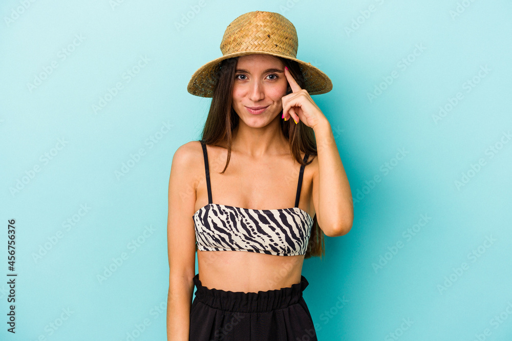 Young caucasian woman going to the beach wearing bikini isolated on blue background pointing temple with finger, thinking, focused on a task. Young caucasian woman going to the beach wearing bikini isolated on blue background pointing temple with finger, thinking, focused on a task.