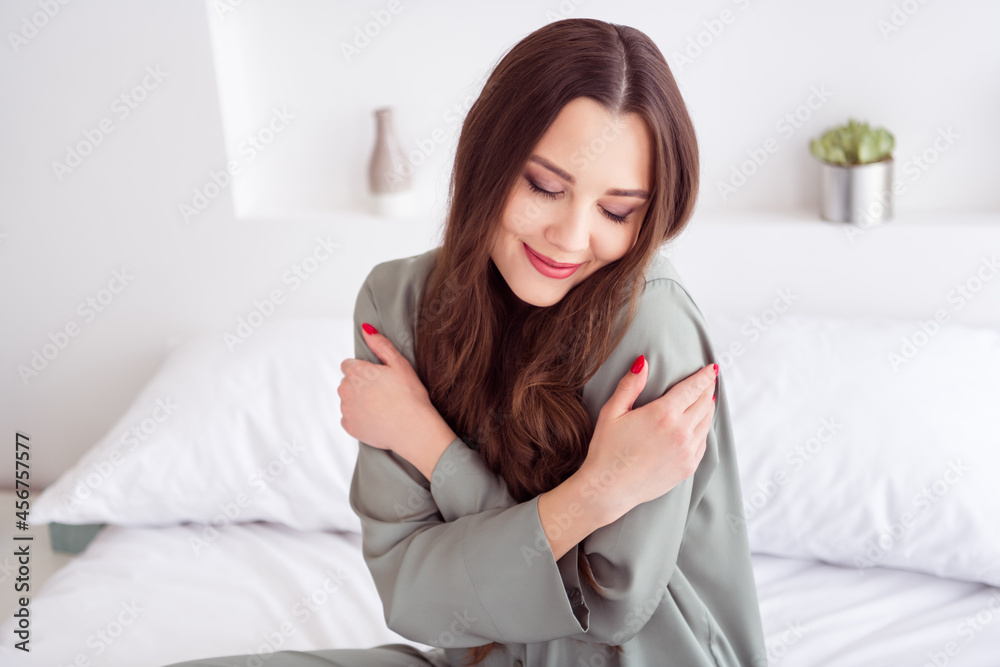 Portrait of attractive dreamy cheerful girl sitting on bed hugging herself enjoying awakening at home house light white interior Portrait of attractive dreamy cheerful girl sitting on bed hugging herself enjoying awakening at home house light white interior