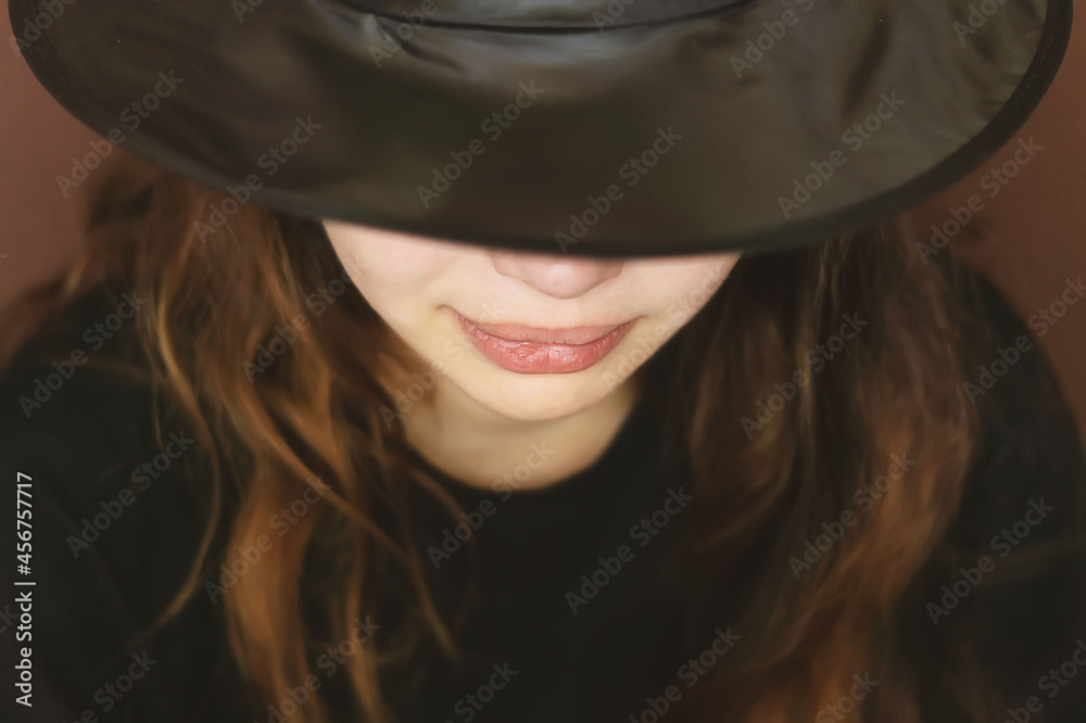 A charming, beautiful, sensual young girl on a dark background with a hat covering half of her face. A dramatic portrait of a young woman in a black wide-brimmed hat. Hidden eyes. Selective focus A charming, beautiful, sensual young girl on a dark background with a hat covering half of her face. A dramatic portrait of a young woman in a black wide-brimmed hat. Hidden eyes. Selective focus