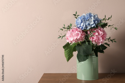 Beautiful hortensia flowers in can on wooden table against beige background. Space for text