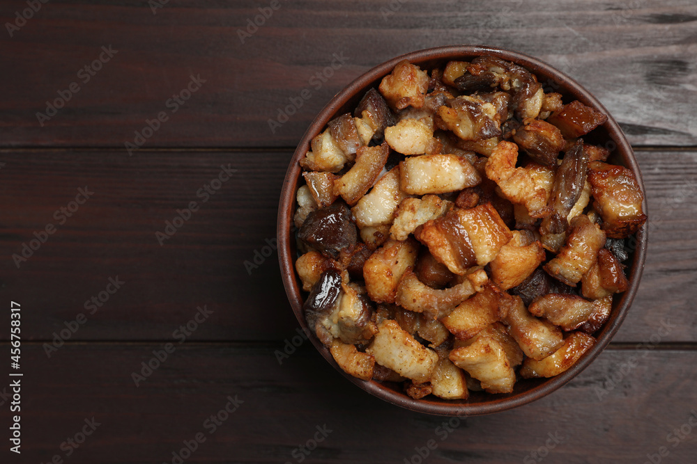 Tasty fried cracklings in bowl on wooden table, top view with space for text. Cooked pork lard Tasty fried cracklings in bowl on wooden table, top view with space for text. Cooked pork lard
