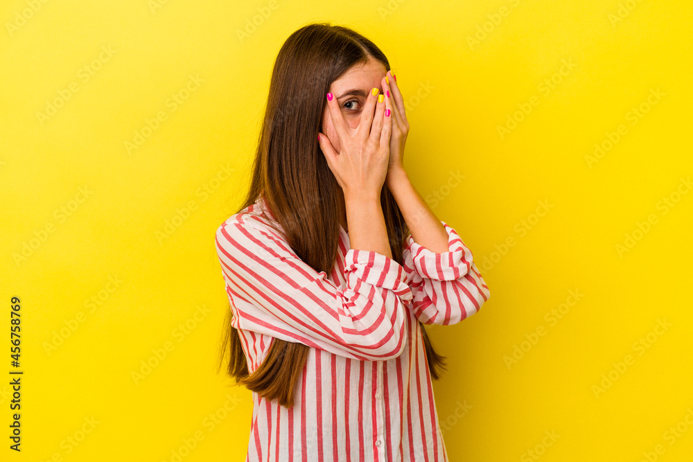 Young caucasian woman isolated on yellow background blink through fingers frightened and nervous. Young caucasian woman isolated on yellow background blink through fingers frightened and nervous.
