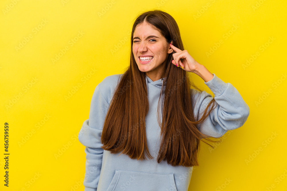 Young caucasian woman isolated on yellow background covering ears with fingers, stressed and desperate by a loudly ambient. Young caucasian woman isolated on yellow background covering ears with fingers, stressed and desperate by a loudly ambient.