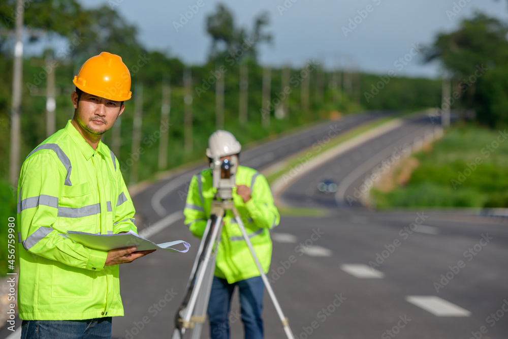 Picture of two civil engineers using theodolites measuring land coordinates standing at outdoor theodolites at a road construction site. Picture of two civil engineers using theodolites measuring land coordinates standing at outdoor theodolites at a road construction site.