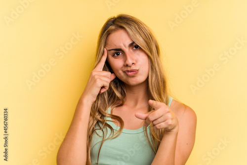 Young caucasian blonde woman isolated on yellow background  pointing temple with finger, thinking, focused on a task.