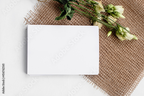 Fashionable white stock background with a blank postcard and flowers. Top view and copy space.