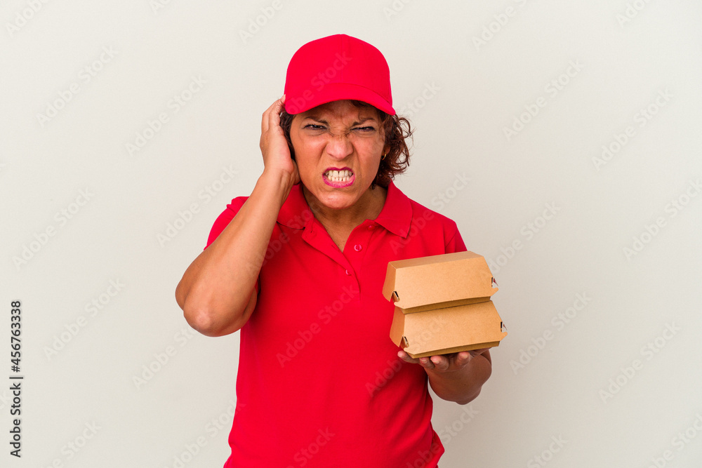 Middle age delivery woman taking burguers isolated on white background covering ears with hands. Middle age delivery woman taking burguers isolated on white background covering ears with hands.