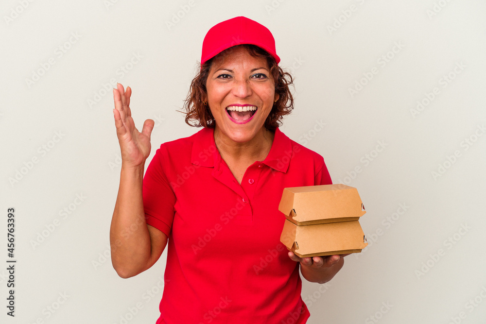 Middle age delivery woman taking burguers isolated on white background receiving a pleasant surprise, excited and raising hands. Middle age delivery woman taking burguers isolated on white background receiving a pleasant surprise, excited and raising hands.