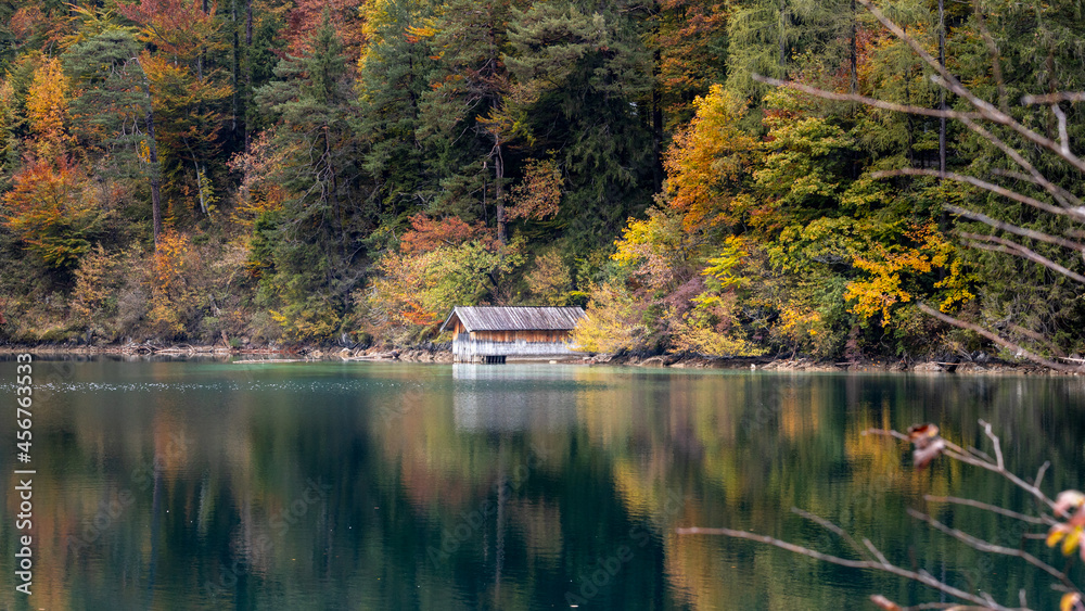 Boathouse and trees with autumn colors reflecting in the lake 
