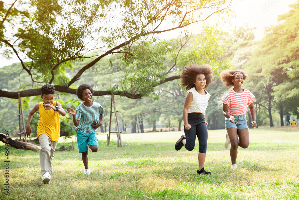 Cheerful kids running in summer day on green grass and many green trees in the park