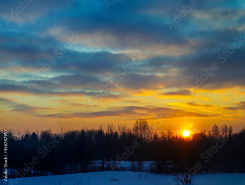 Sunset in winter forest. Sunbeams through snow-covered trees. Beautiful natural landscape on a frosty evening.