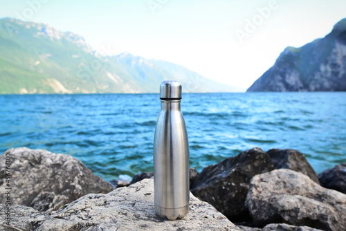 Steel water bottle on the background of the lake in the mountains. Riva del Garda. Copy space concept.