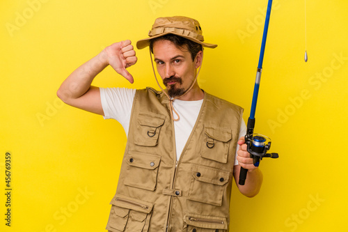 Young caucasian fisherman holding rod isolated on yellow background feels proud and self confident, example to follow.