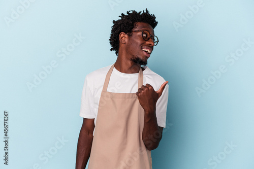 Young african american store clerk isolated on blue background points with thumb finger away, laughing and carefree Fotobehang