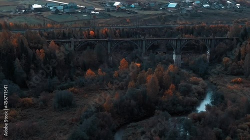 An old viaduct across the river against the backdrop of an autumn yellowing forest near the railway. The abandoned viaduct is removed from the Drone, the throne approaches and flies over the viaduct. photo