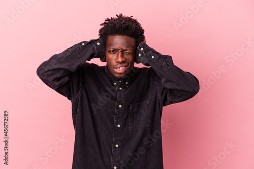 Young african american man isolated on pink background covering ears with hands.