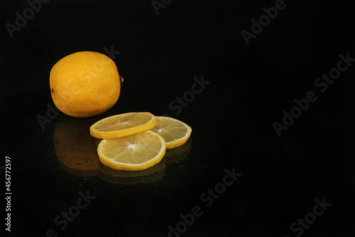 Sliced lemon slices on a black background, reflection in the glass