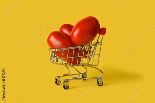 Mini shopping basket with tomatoes isolated on yellow background. Retail. Sales concept.