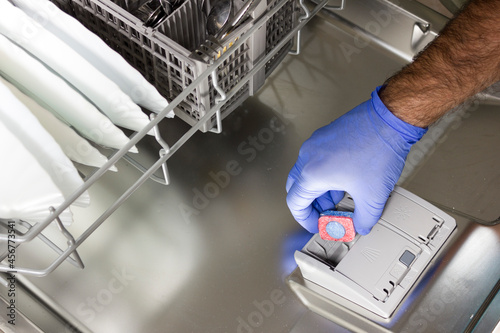 View from above of a man's hand depositing the detergent tablet into the dishwasher