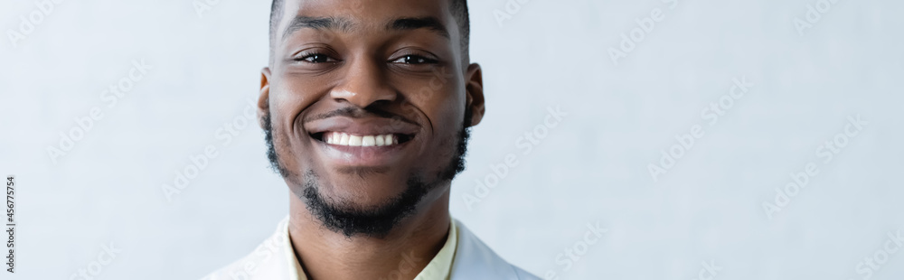 young and happy african american doctor smiling at camera on white background, banner