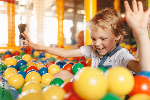 School children having fun in indoor park playground. Happy boy playing at balls pool playground. Boys and girls playing with multi colored plastic balls in big dry paddling pool in playing centre