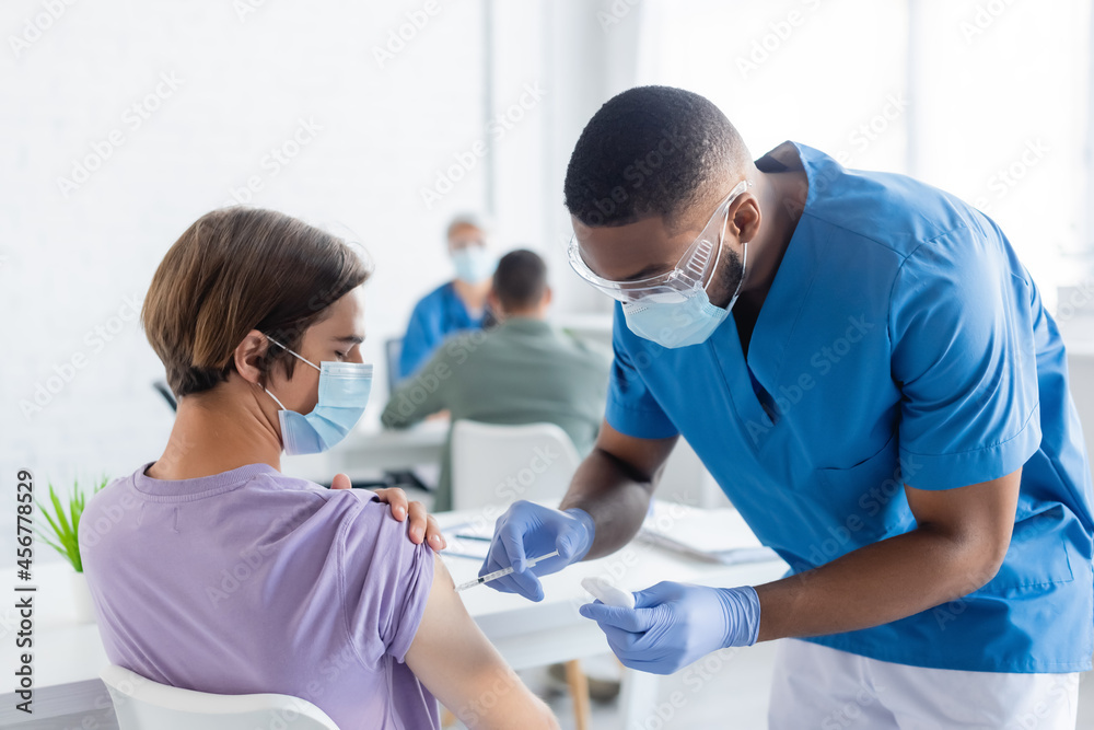 Obraz premium african american physician in medical mask and goggles vaccinating man in clinic