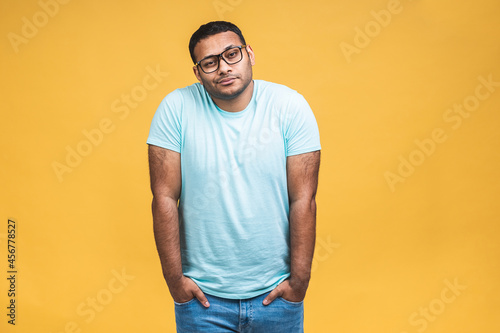 Portrait of a serious thinking young african american indian black man standing isolated over yellow background.