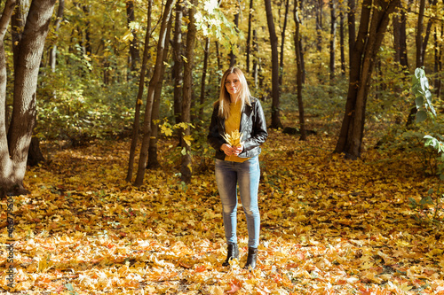 Portrait of beautiful woman holds autumn leaves. Stylish youth and fall season concept.