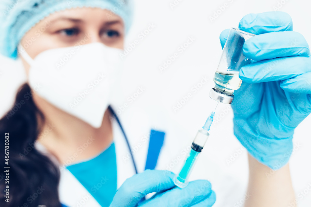 A female doctor in a medical face mask and gloves dials the vaccine into a syringe from an ampoule. Medical worker close-up. Vaccination against infectious and colds. A female doctor in a medical face mask and gloves dials the vaccine into a syringe from an ampoule. Medical worker close-up. Vaccination against infectious and colds.