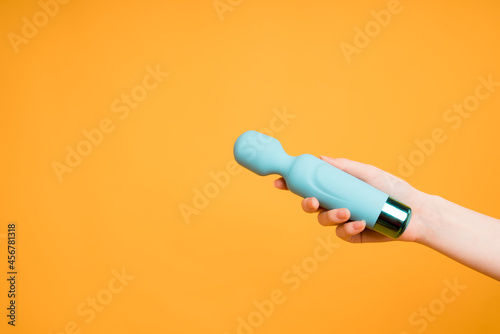 A blue vibrator for stimulating orgasm lies in a woman's hand on a yellow background.Useful for a sex shop