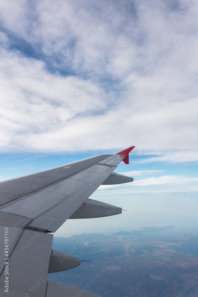 Airplane flying under cloudy sky over ocean and land Airplane flying under cloudy sky over ocean and land