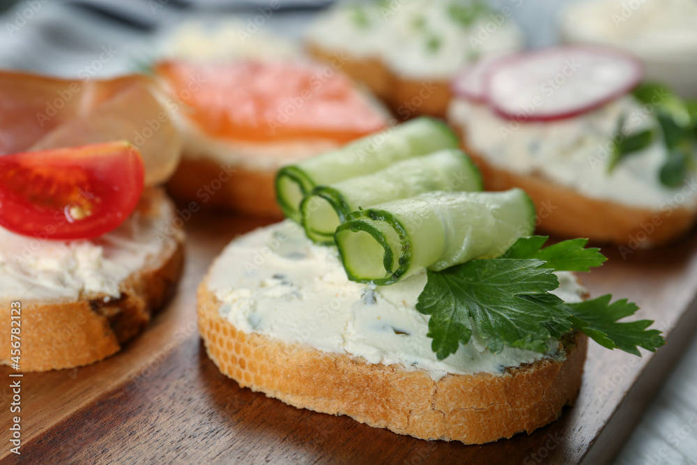 Toasted bread with cream cheese, cucumber and parsley on wooden board, closeup