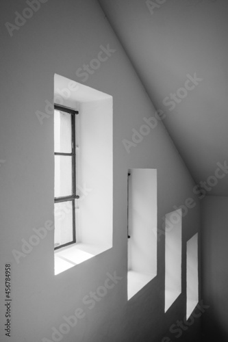 Interior view, moody black and white tone, 3 square windows arrange on the wall of stairway. 