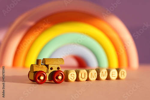 a wooden train with cubes with the inscription summer on the background of a voluminous bright rainbow