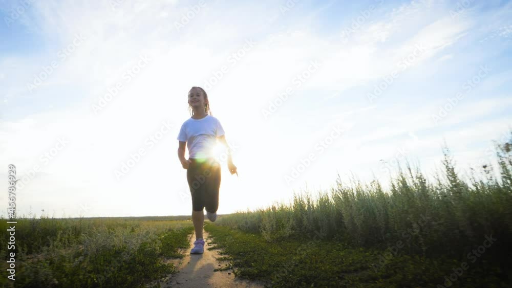 Happy childhood. Cheerful girl are running in the green meadow. Back view of girl running on flower meadow at evening twilight. Teen girl running on meadow with sunset. Happy family concept. Happy childhood. Cheerful girl are running in the green meadow. Back view of girl running on flower meadow at evening twilight. Teen girl running on meadow with sunset. Happy family concept.