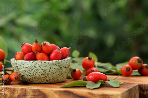 Ripe rose hip berries with green leaves on wooden table. Space for text