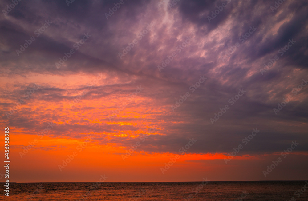 Dramatic overcast clouds, pink sunrays, and reflective ocean surface at dawn on Cape Cod in the summer