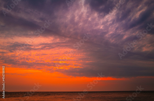 Dramatic overcast clouds, pink sunrays, and reflective ocean surface at dawn on Cape Cod in the summer © Naya Na
