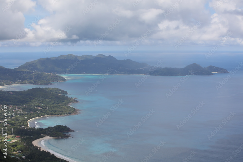 Tropical island in the ocean with winding coastline with beach and beautiful sky with clouds.Aerial view of land with mountains and turquoise water in fog of Seychelles.Cloudy rainy seascape