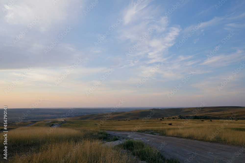 Peaks of hills with steppe grass. Sunset sky and feather clouds.