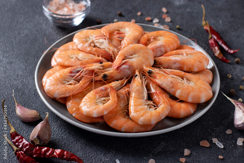 Boiled shrimps in a round plate and spices on a dark background. Closeup Boiled shrimps in a round plate and spices on a dark background. Closeup