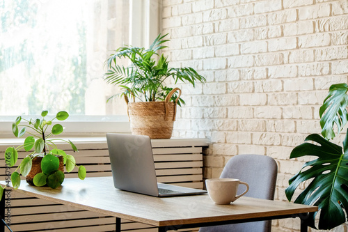 Creative workspace of a blogger. Laptop computer on wooden table in loft style corner office with brick walls and big windows. Designer's table concept. Close up, copy space, background.