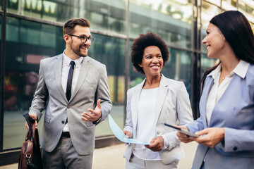 Three young business people talking to each other while walking outdoors.