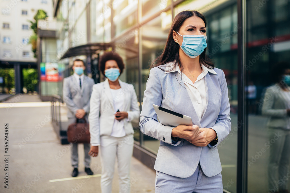Business people with protectiveface mask waiting in line on a safe distance during COVID-19 epidemic.